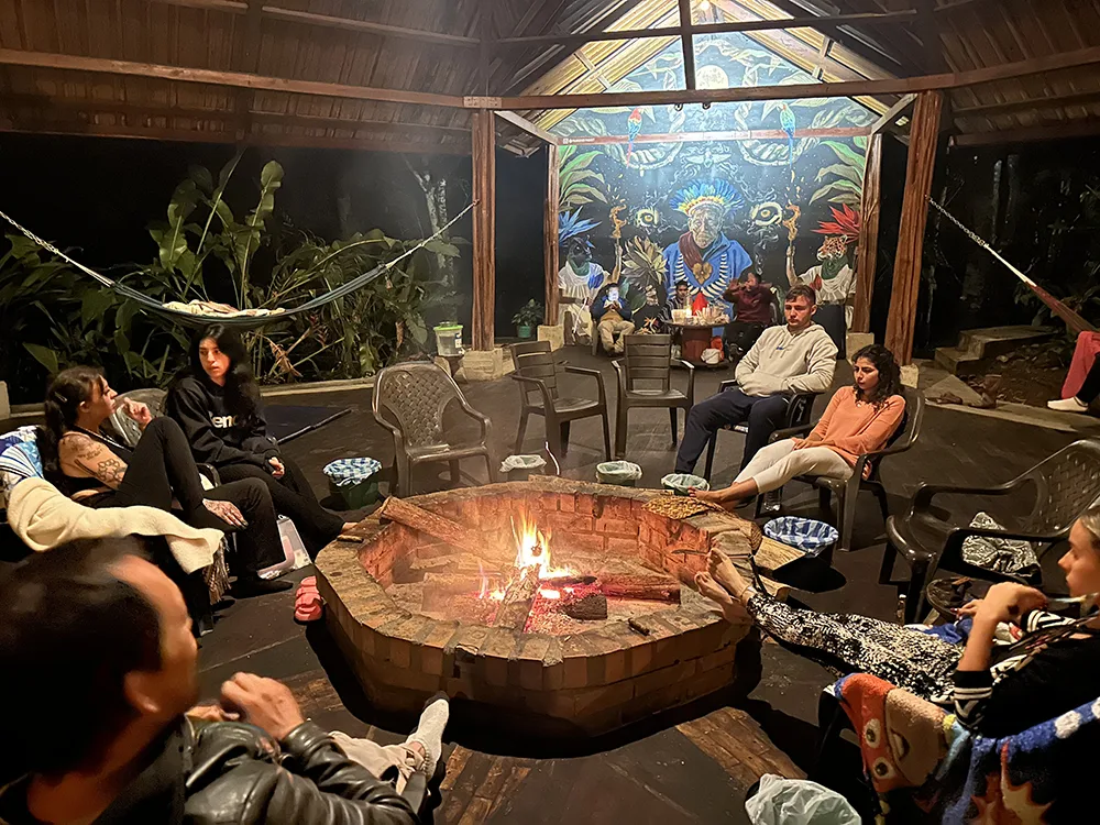 Group of participants seated around a fire in a covered communal space during an ayahuasca retreat in Colombia.