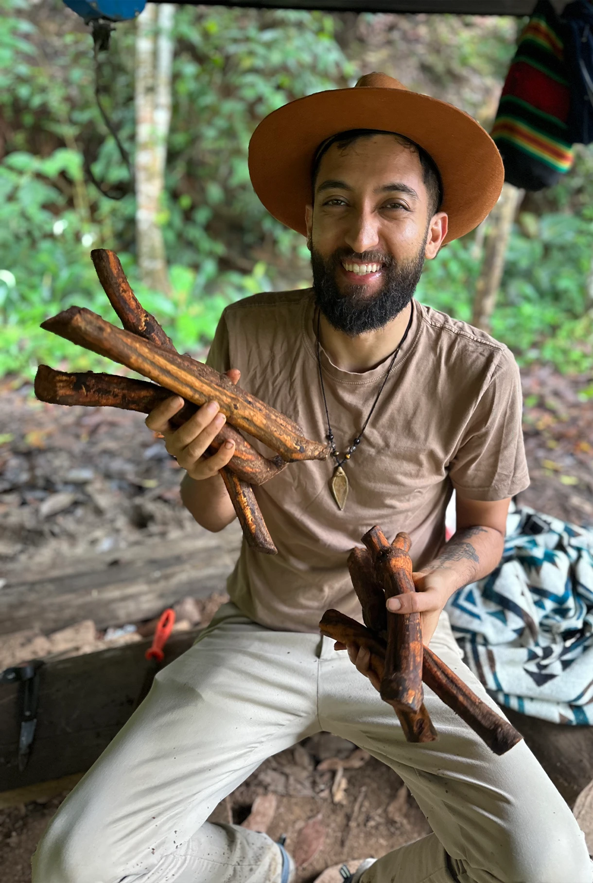 Yasha, founder of MahaDevi Ayahuasca, holding ayahuasca vine in a forest setting in Colombia.